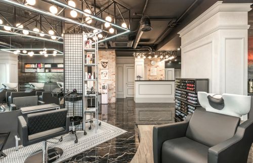 Backwash chair with sink placed near shelves with cosmetology products and reception desk in stylish beauty salon with decorated walls