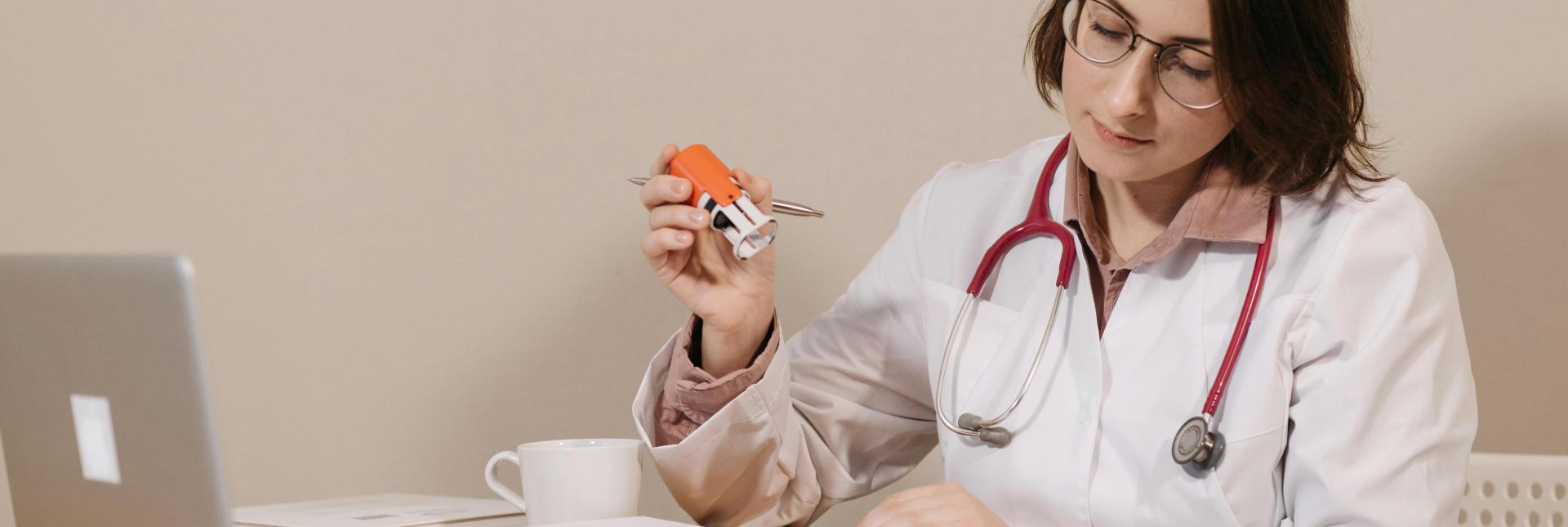A focused female doctor reviews medical documents while sitting at her desk with a stethoscope.